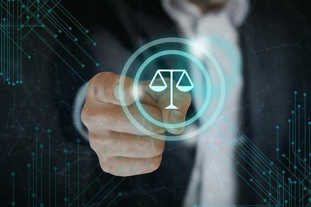 A businessman points at a glowing digital icon of justice scales, symbolizing legal technology or compliance, with a futuristic network background.